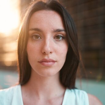Close-up portrait of young woman with freckles and dark loose hair and long eyelashes at the camera
